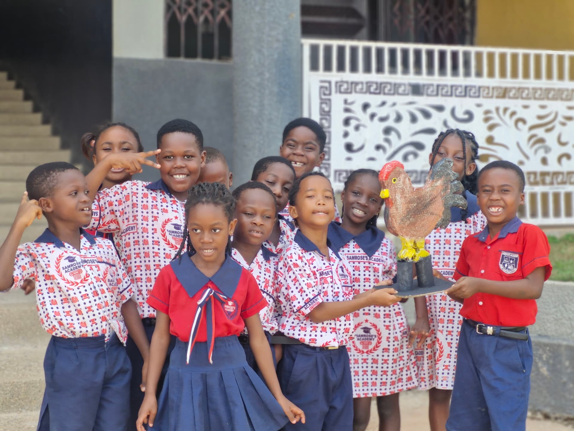 Primary pupils holding a handcrafted rooster sculpture outside the campus